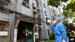 Seorang relawan menggunakan megafon ketika berbicara dengan para warga di sebuah komplek apartemen di Shanghai, China, di tengah lockdown yang diberlakukan di wilayah tersebut, pada 12 April 2022. (Foto: Xinhua via AP/Chen Jianli)