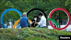 路人在坐落在日本奥委会总部附近的奥运五环徽标前闲谈。（路透社2021年6月23日照片）