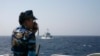 FILE - An officer of the Vietnamese coast guard officer speaks on a radio as he monitors a Chinese vessel (top) in the South China Sea, about 210 km (130 miles) off Vietnam's shore.