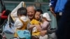 FILE - An elderly man plays with children near a commercial office building in Beijing on May 10, 2021.