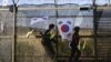 Tentara Korea Selatan berjaga-jaga di sekitar Paviliun Imjingak, mengibarkan bendera dan pita nasional sambil mengekspresikan harapan akan reunifikasi Korea. Lokasi ini, berada di dekat Panmunjom, zona demiliterisasi yang memisahkan kedua Korea sejak Perang Korea. 